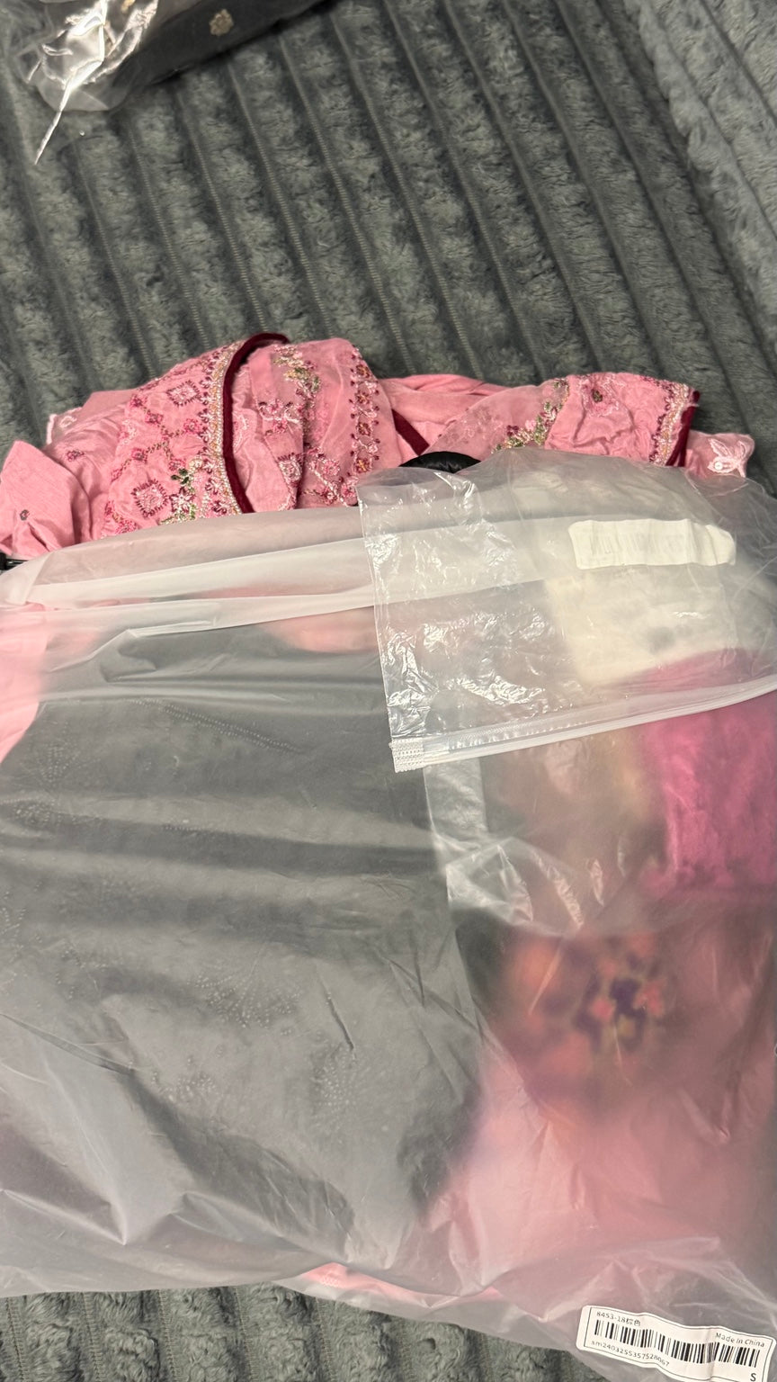 Pink embroidered occasion garment with decorative trim, partially visible in packaging